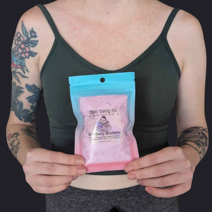 A person holding a small resealable pouch of cloud candy strawberry shortcake cotton candy against a dark background. The pouch has a bright blue top seal and a printed label reading 'Cloud Candy Co' and 'Strawberry Shortcake'.