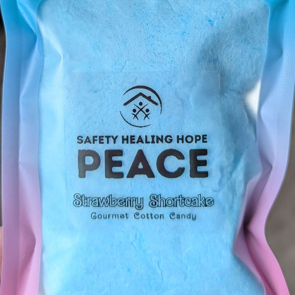 A package of 'Peace' strawberry shortcake gourmet cotton candy by Safety Healing Hope, featuring light blue cotton candy inside a clear windowed resealable pouch with a blue and pink gradient design.